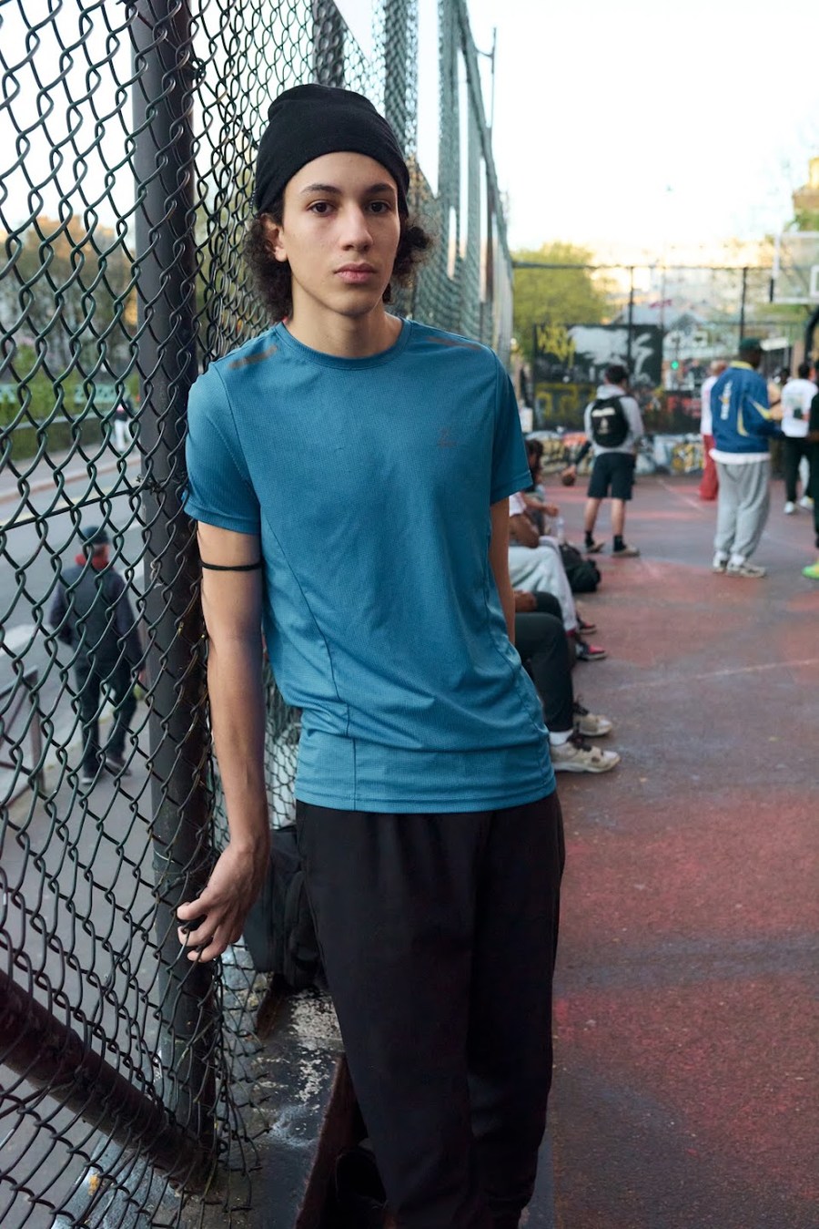 Portrait in a blue T-shirt beside the basketball court fence