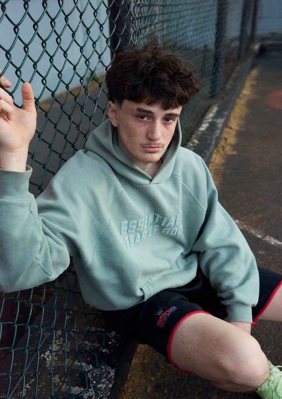 Portrait in a pale green hoodie leaning against the fence