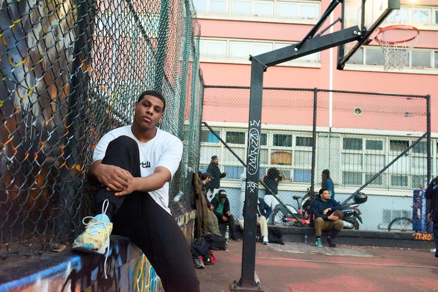 Seated figure beside the fence with basketball players in the background