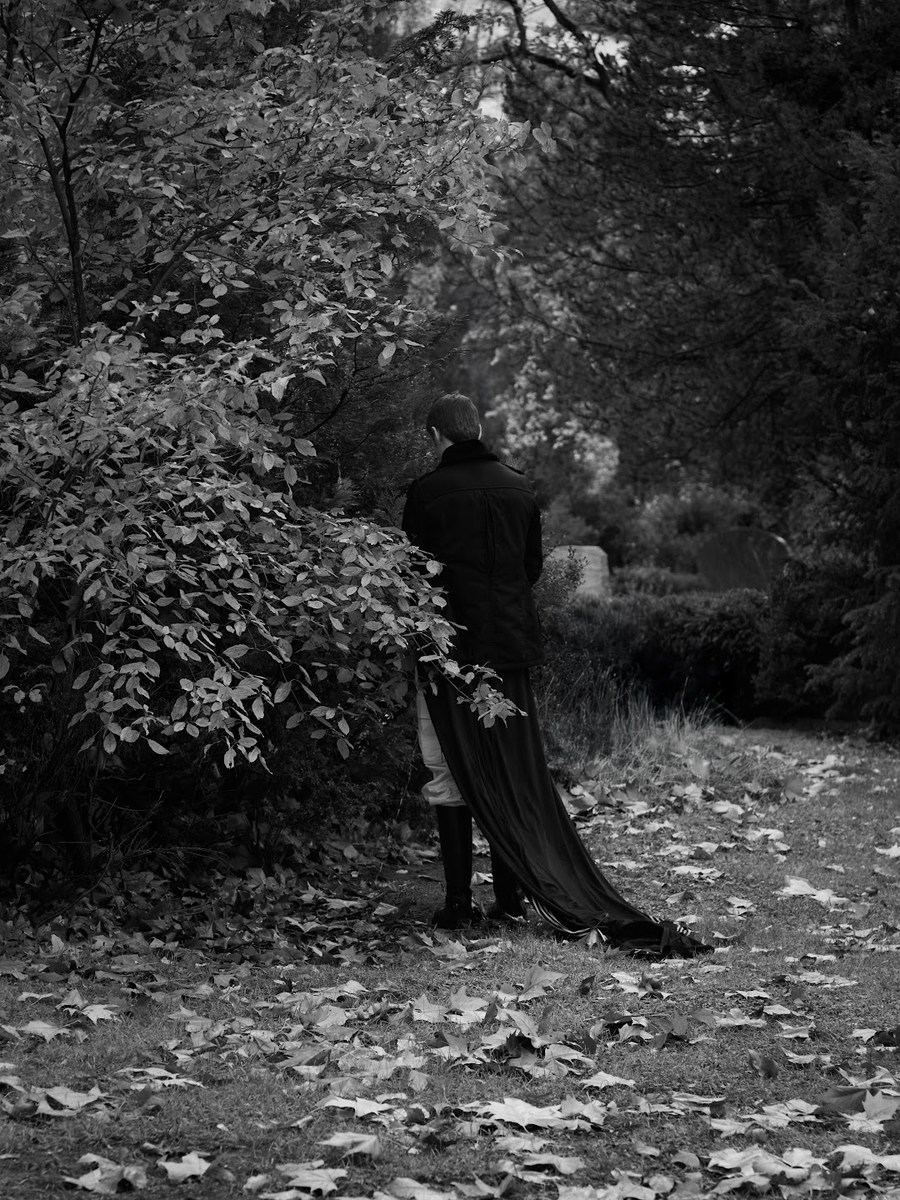 Black-and-white photograph of a figure in dark clothing beneath trees