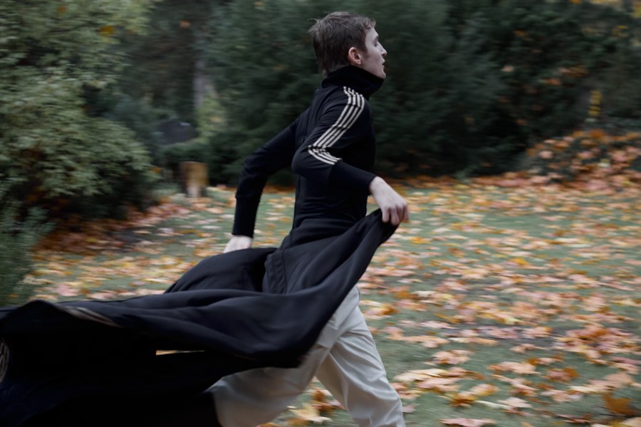 Figure running through autumn woodland with a long black garment trailing behind