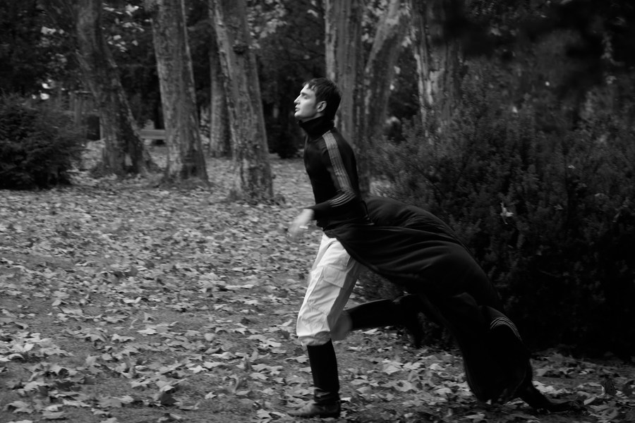 Black-and-white photograph of a figure moving through woodland with fabric trailing behind