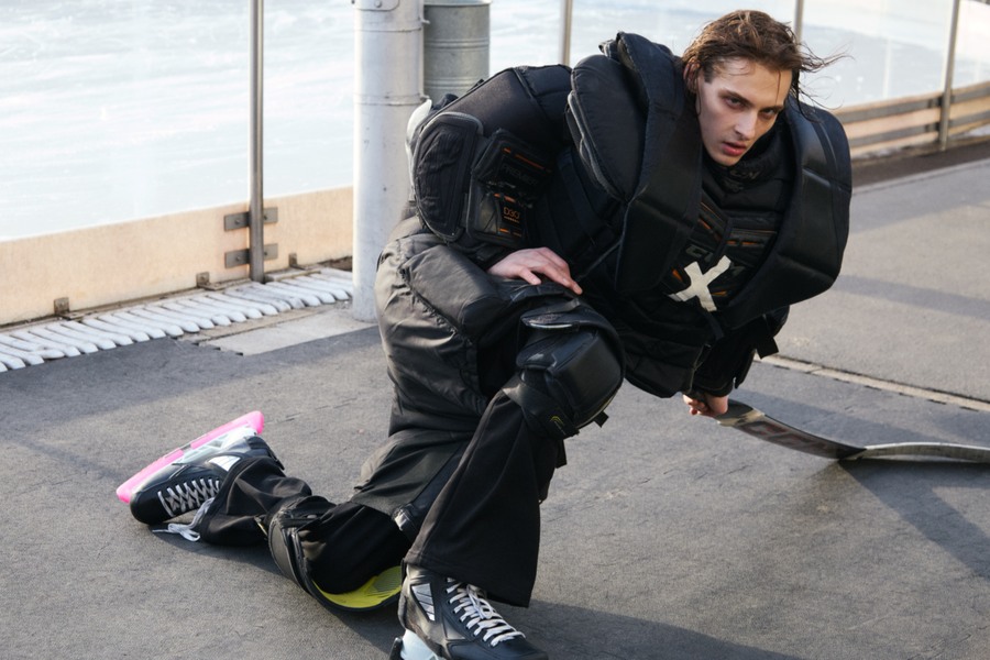 Marks seated low beside the rink boards in black padding and pink skate guards
