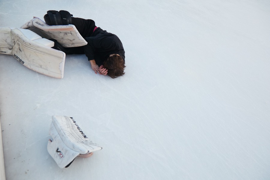 Marks lying curled on the ice beside white goalkeeper pads