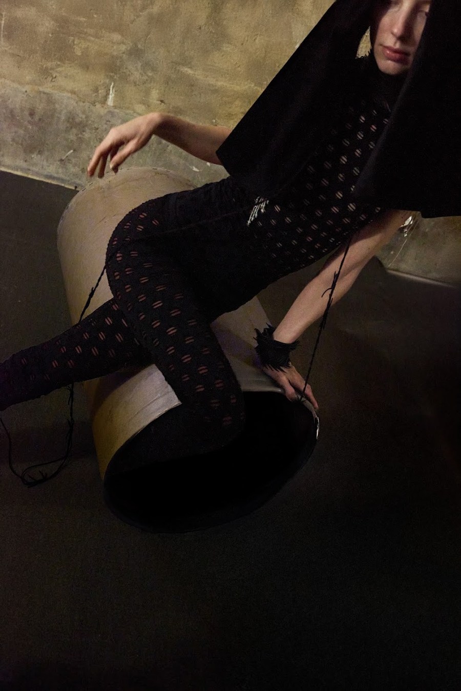 Model seated on a tube in black clothing and a hood