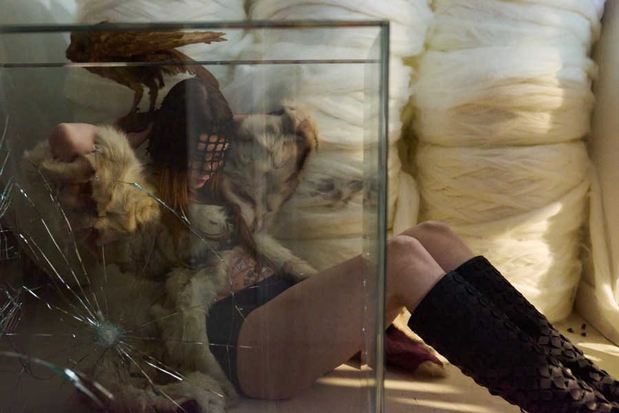 Model reclining behind cracked glass, beside large rolls of white fibre