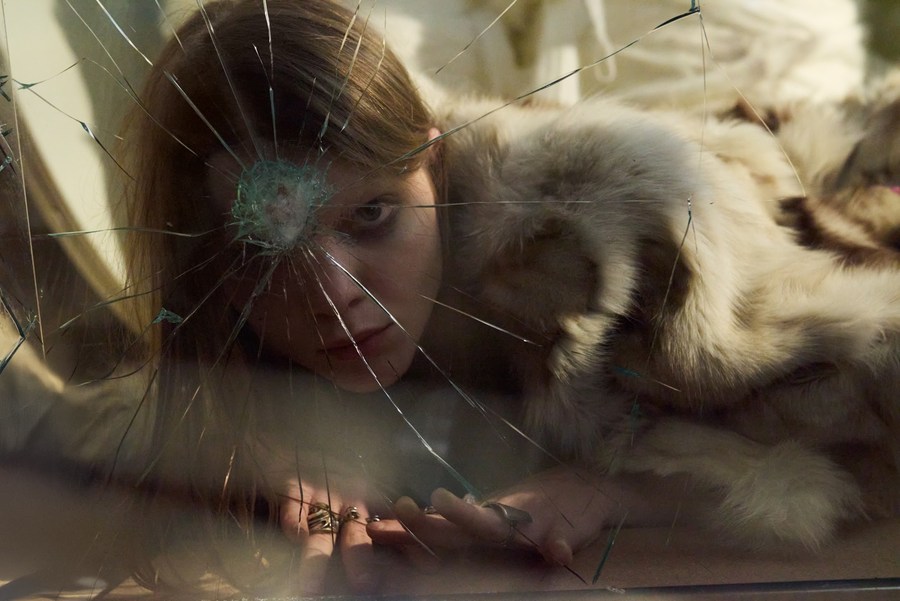 Red-haired model beside a fur hood, seen through cracked glass