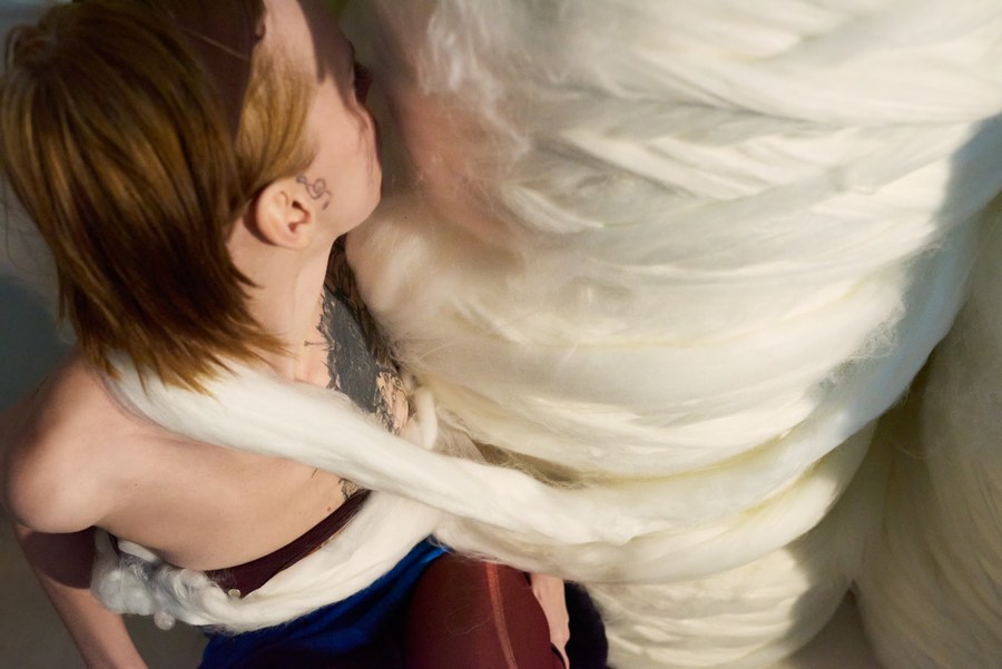 Model wrapped in soft white material beside large rolls of fibre